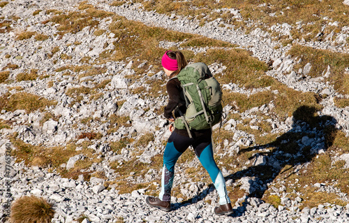 Young woman in hiking boots with big green backpack trekking in rocky mountains, Autumn vibes in mountain range Hochschwab, Styria, Austrian Alps, Europe. Freedom and wilderness. Golden slopes.