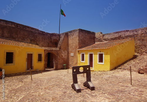 Castro Marim castle, with medieval stocks and yellow buildings at background.