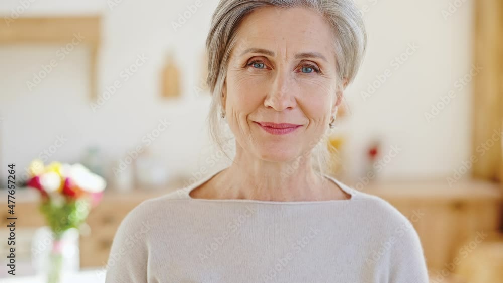Natural beauty of aging. Peaceful positive senior lady looking at camera, posing at home interior with flowers bouquet
