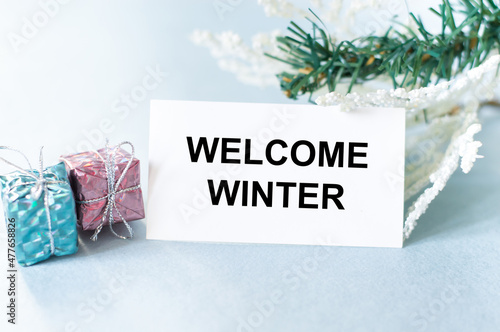 hello winter word on a white business card on a light background next to two gifts in a package and spruce branches