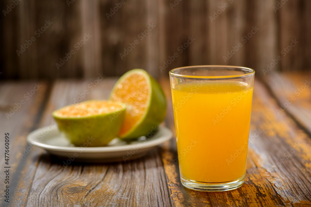 Fototapeta premium Orange juice. Glass on wooden table with a sliced orange in the background.