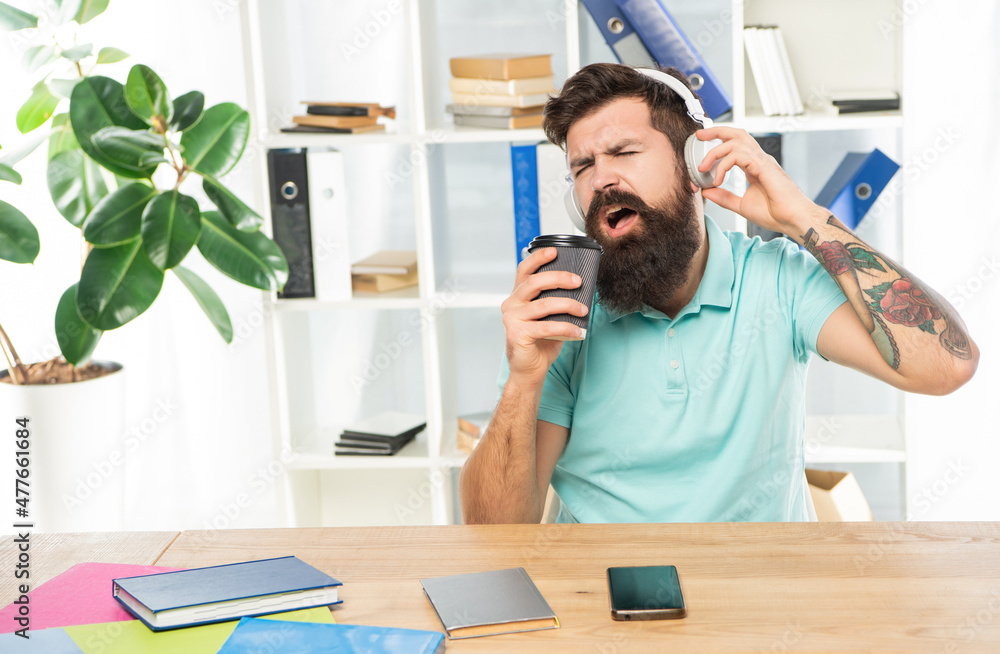 Happy man singing to takeaway cup listening to song in headphones in office, music