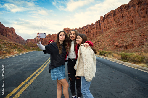 Three teen girls taking a selfie photo together outdoors with beautiful scenic red cliffs in the background.