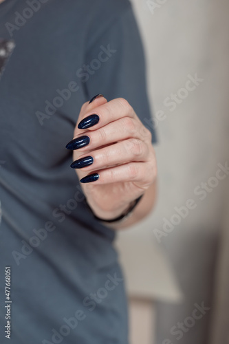 Female hand with long nails and dark blue teal manicure holds a bottle of nail polish © Tatiana