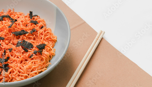 Korean instant noodles menu in a white bowl on brown paper with chopsticks on the side, close-up shot against a white background. Used in food and health applications