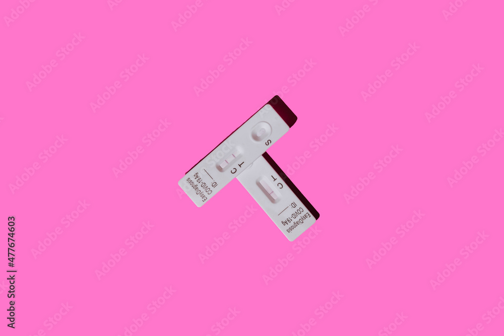 Overhead view of two covid-19 antigen rapid diagnostic test devices, the top one with a positive result and the bottom one with a negative result, on a pink background Overhead view of two covid-19 antigen rapid diagnostic test devices, the top one with a positive result and the bottom one with a negative result, on a pink background