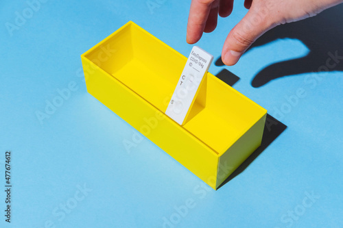 A hand picking up a rapid antigen test for the diagnosis of COVID-19 with a negative result that is inside a yellow box, on a blue background.