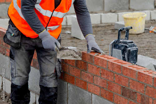 Foto Bricklayer laying bricks on mortar on new residential house construction