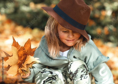 happy smiling girl in brown hat playing with leaves in autumn park 