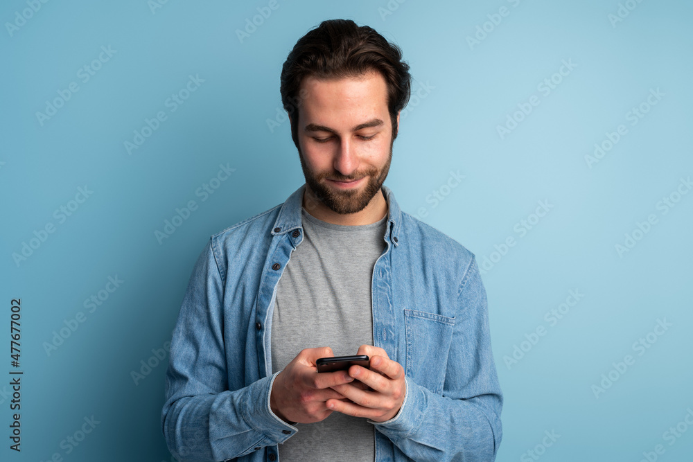 Cheerful brunette man with beard using cellphone and smiling, reading good news message