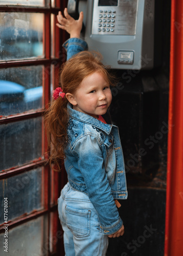 smiling red hair girl in jeans costume trying to talking on the phone in English classic red box  