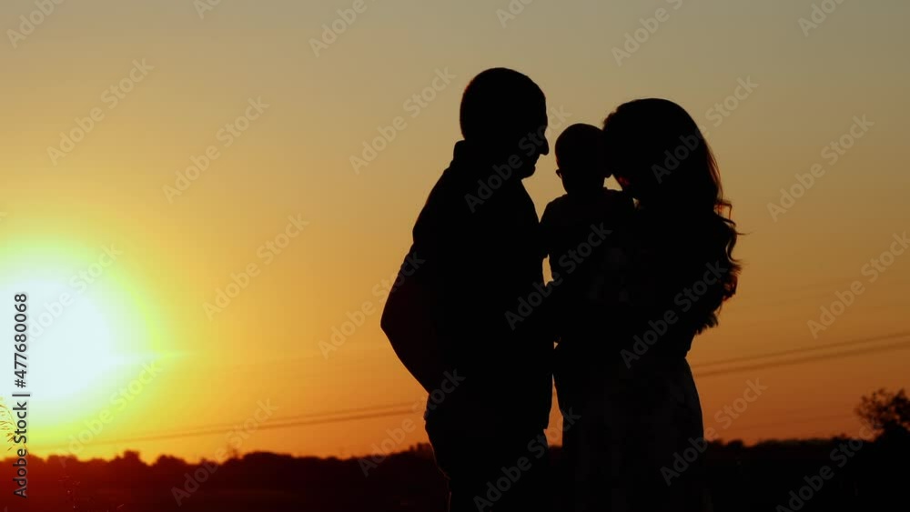 Unrecognizable silhouette of family at sunset, parents hug and kiss their child, family values and parental love Unrecognizable silhouette of family at sunset, parents hug and kiss their child, family values and parental love