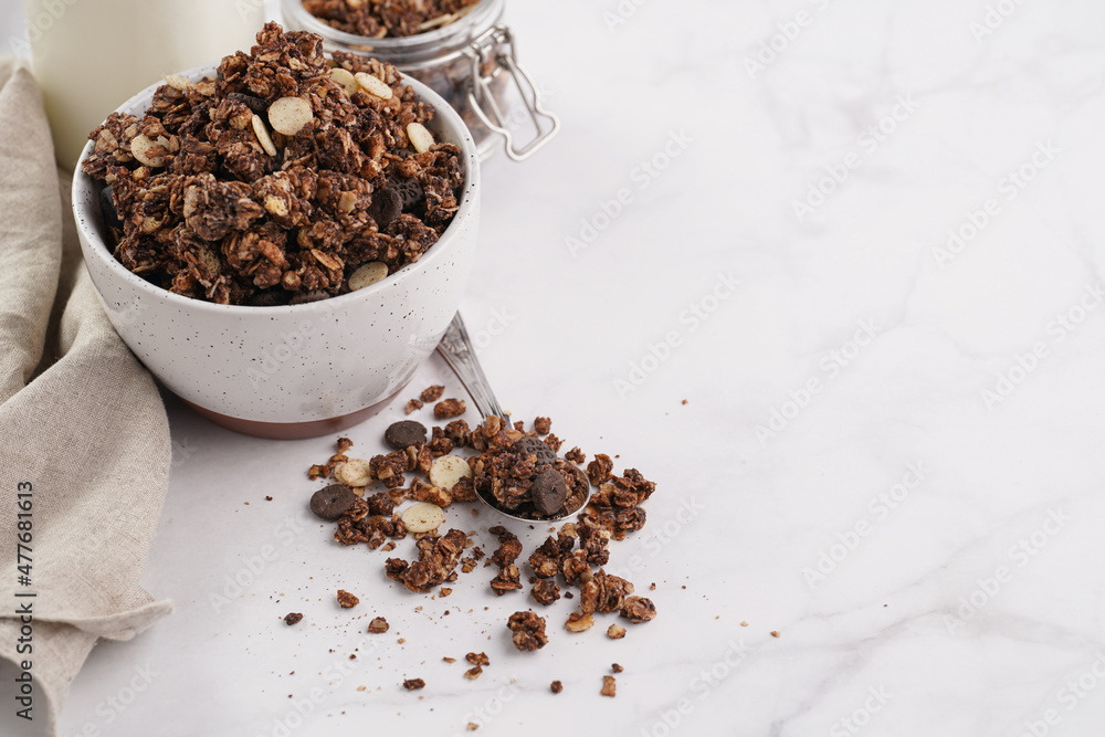 Breakfast muesli cereal with chocolate chips and nuts in several jars and bowl, bottle of milk, white surface Breakfast muesli cereal with chocolate chips and nuts in several jars and bowl, bottle of milk, white surface