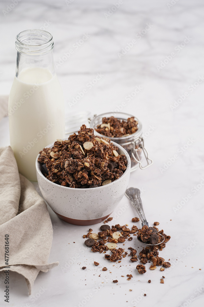 Breakfast muesli cereal with chocolate chips and nuts in several jars and bowl, bottle of milk, white surface Breakfast muesli cereal with chocolate chips and nuts in several jars and bowl, bottle of milk, white surface