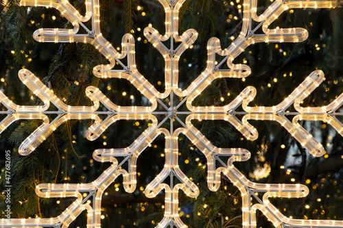 Close-Up Of Illuminated Snowflake Against christmas tree Background © ArieStudio