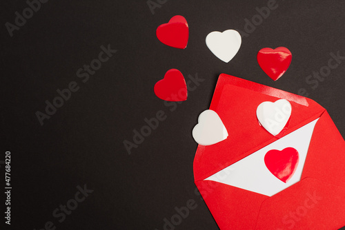 top view of red envelope with love letter and paper cut hearts isolated on black.