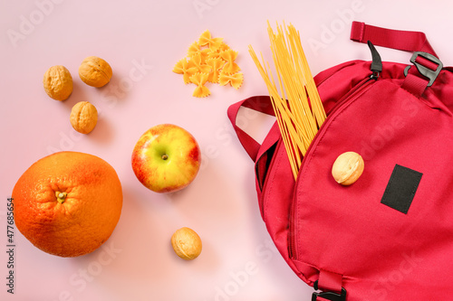 Red backpack with various pasta, fruits and nuts on pink background. Food delivery concept, shopping, tourist food photo