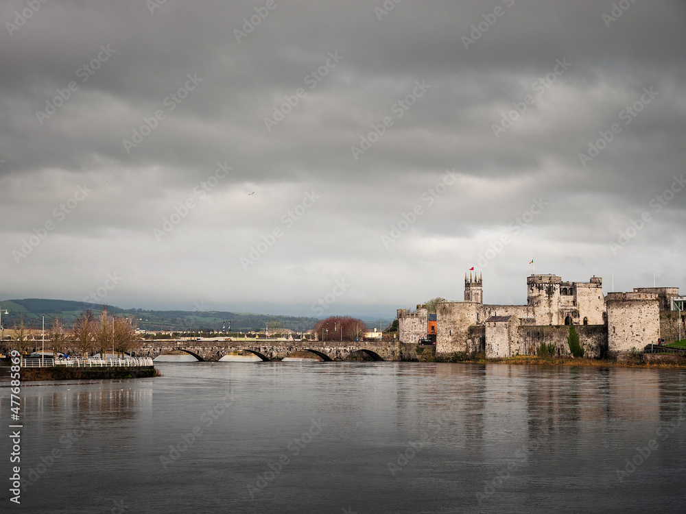 King Jonh's castle on River Shannon, Limerick city, Ireland. Popular museum and landmark. Fine example of stone stronghold with tall walls and towers. Cloudy sky. Building reflection in water.