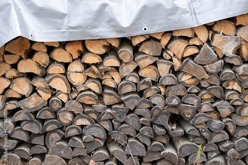 Stacked woodpile for firewood under grey tarp. 