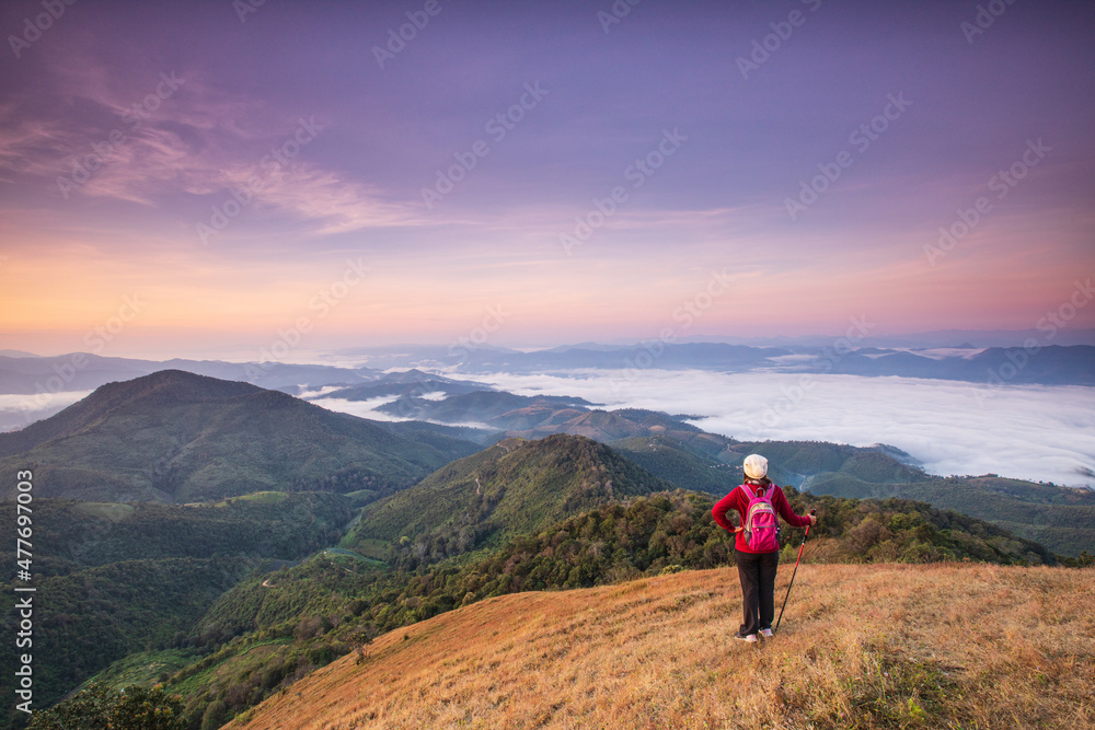 Young  woman in red jacket hiking on high mountains and sea of mist . Doi Pui Ko,  Mae Hong Son Province, Thailand.