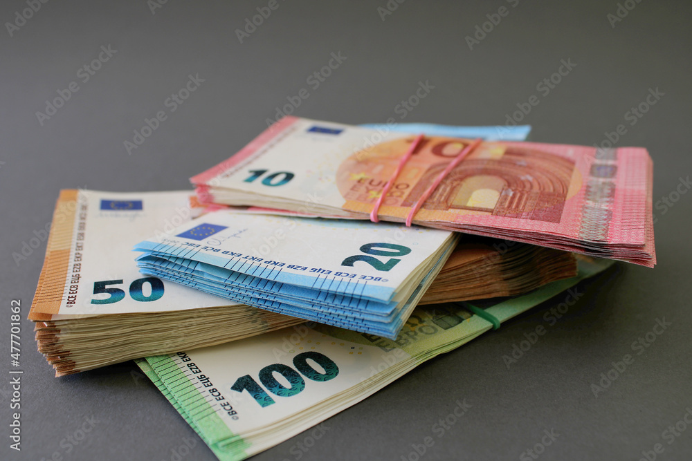 Stacks of 10, 20, 50 and 100 euro banknotes, tied with rubber band and lying one on one, isolated on a grey background. Euro money. Close up view. Stacks of 10, 20, 50 and 100 euro banknotes, tied with rubber band and lying one on one, isolated on a grey background. Euro money. Close up view.