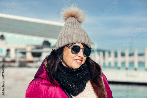 portrait of a smiling woman with sunglasses and wool cap on a sunny autumn day walking in the city