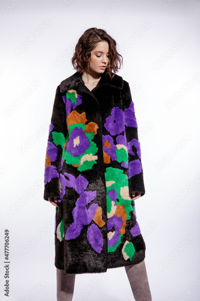 High fashion photo of a beautiful elegant young woman in a pretty black fur coat with colorful patterns, suede boots posing over white background. Make up, hairstyle. Slim figure. High fashion photo of a beautiful elegant young woman in a pretty black fur coat with colorful patterns, suede boots posing over white background. Make up, hairstyle. Slim figure.