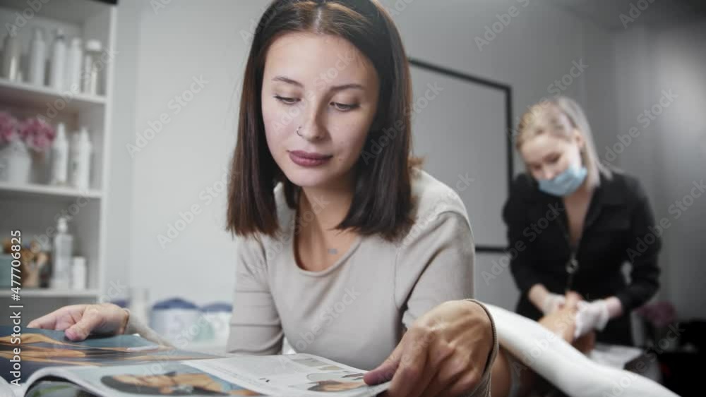 Blonde depilation master removing hairs from the leg on her woman client while she's lying on a couch and reading a magazine Blonde depilation master removing hairs from the leg on her woman client while she's lying on a couch and reading a magazine