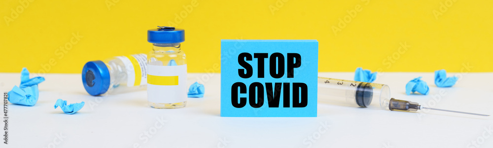 On the table is a syringe, injections and a blue sign with the inscription - STOP COVID On the table is a syringe, injections and a blue sign with the inscription - STOP COVID