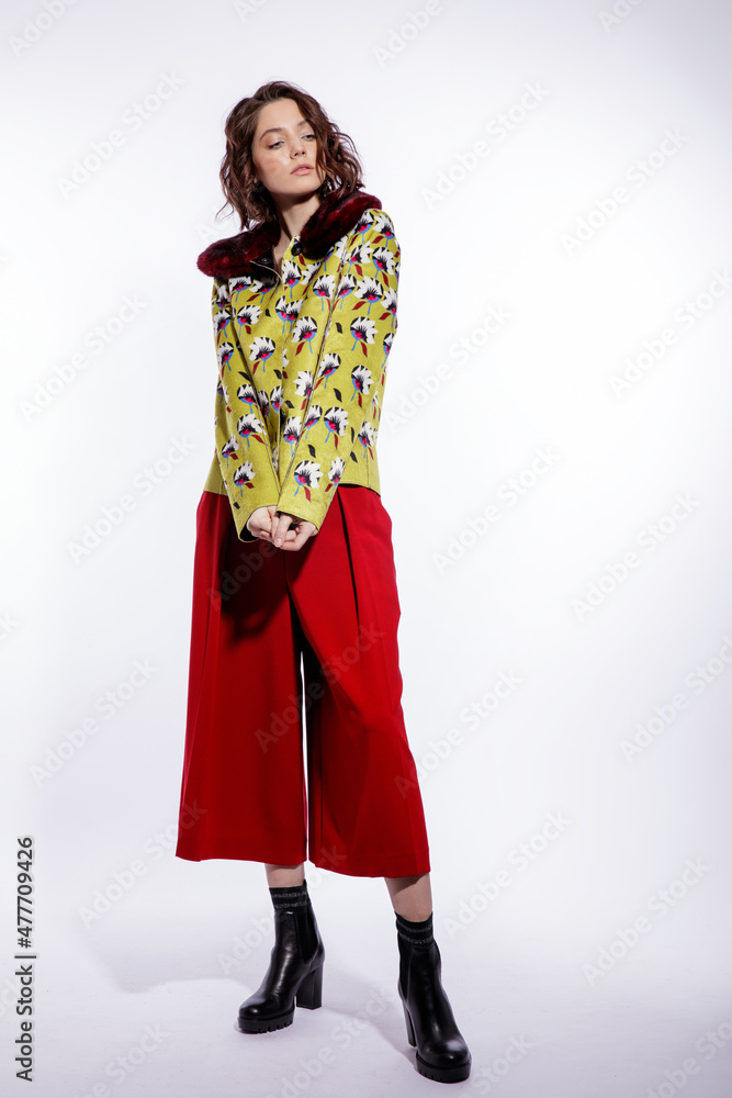 High fashion photo of a beautiful elegant young woman in a pretty yellow jacket with pattern flowers, red trousers, pants posing over white background. Make up, hairstyle. Slim figure. Studio shot High fashion photo of a beautiful elegant young woman in a pretty yellow jacket with pattern flowers, red trousers, pants posing over white background. Make up, hairstyle. Slim figure. Studio shot