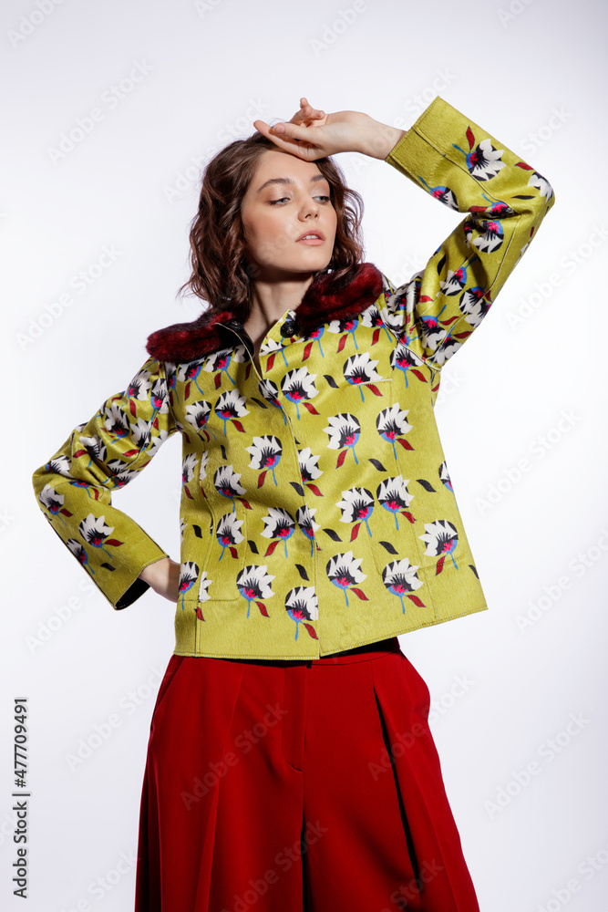 High fashion photo of a beautiful elegant young woman in a pretty yellow jacket with pattern flowers, red trousers, pants posing over white background. Make up, hairstyle. Slim figure. Studio shot High fashion photo of a beautiful elegant young woman in a pretty yellow jacket with pattern flowers, red trousers, pants posing over white background. Make up, hairstyle. Slim figure. Studio shot