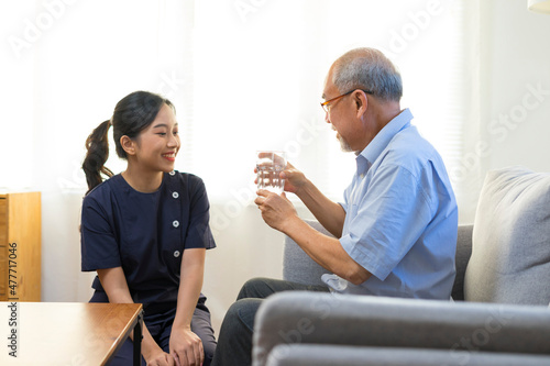 Smiling nurse giving glass of water to senior asian man in nursing home or assisted living facility. © bennnn