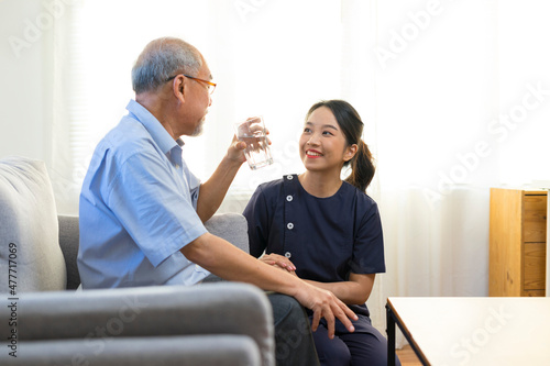 Smiling nurse giving glass of water to senior asian man in nursing home or assisted living facility. © bennnn