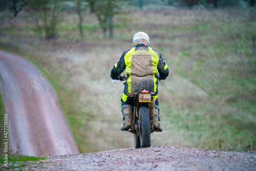 a motor cyclist (biker) wearing a bright yellow hi-vis jacket, back covered in mud, riding his off-road motorbike along a stone track on Salisbury Plain, Wiltshire