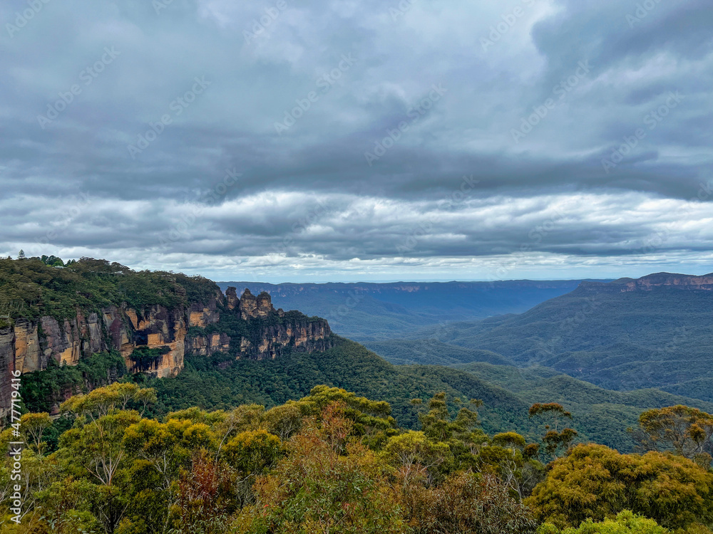 The Three Sisters rocks at Blue Mountains with view of dark clouds covering the rainforest trees, Sydney Australia.