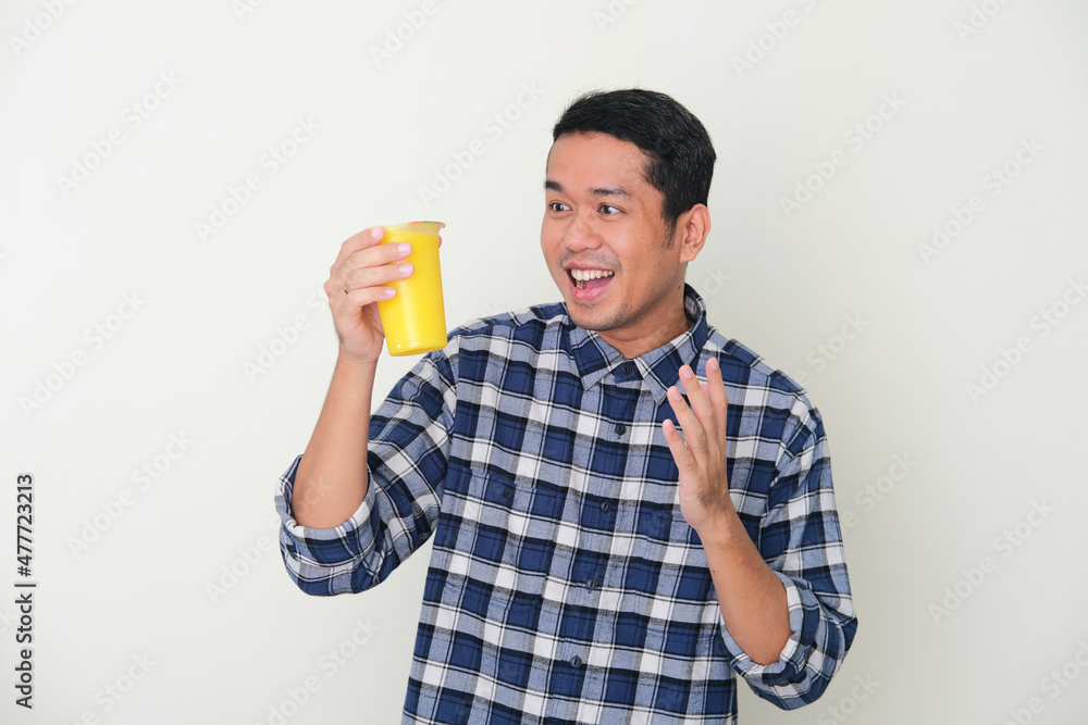 Adult Asian man showing happy face when looking to a cup of cold yellow fruit juice drink Adult Asian man showing happy face when looking to a cup of cold yellow fruit juice drink