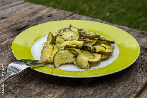 Zucchini Salat auf einem grünen Teller mit einer Gabel, draußen auf einem rustikalen Tisch im Garten