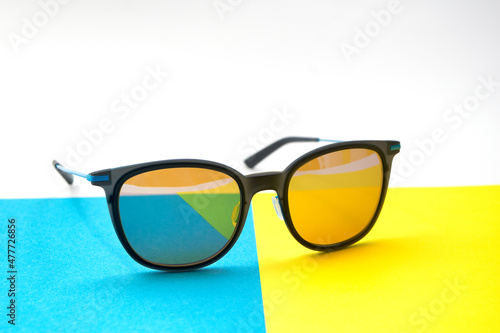 Conceptual elegant Sunglasses on blue, yellow and white background. Sun glasses summer accessories as design element for promo or advertising.
