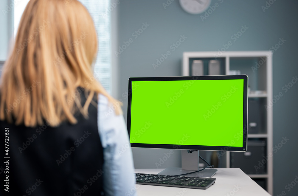 Back view of mature woman in formal wear sitting at office desk and working on modern computer. Focus on green empty monitor. Back view of mature woman in formal wear sitting at office desk and working on modern computer. Focus on green empty monitor.