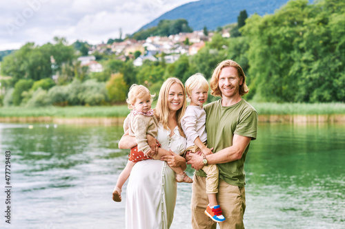 Outdoor portrait of beautiful family, young couple with preschooler boy and toddler girl posing next to lake or river © annanahabed