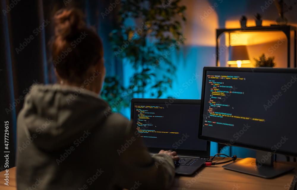 Caucasian woman working with two modern computers for design and coding program. Female programmist sitting at home office during evening time. Caucasian woman working with two modern computers for design and coding program. Female programmist sitting at home office during evening time.