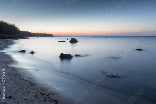 Scenic view to the coastal  sandy beach with erratic rocks in the water and the sunset colored sea and sky background