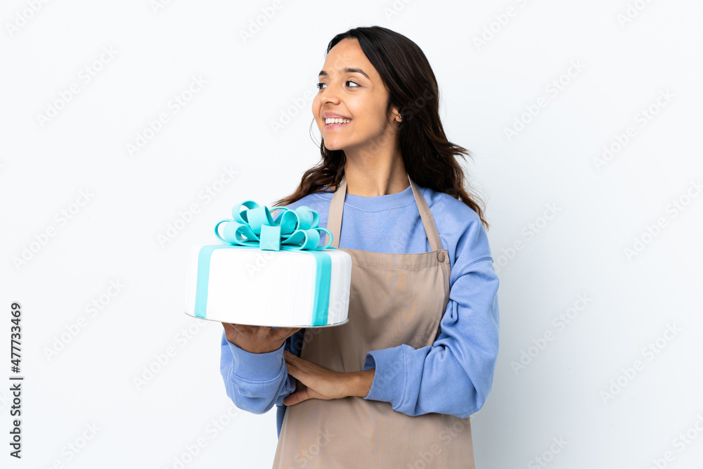 Pastry chef holding a big cake over isolated white background looking side Pastry chef holding a big cake over isolated white background looking side