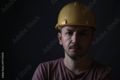 Dirty miner in yellow helmet on dark background. Portrait of face close up. photo