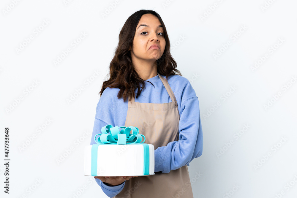 Pastry chef holding a big cake over isolated white background making doubts gesture while lifting the shoulders Pastry chef holding a big cake over isolated white background making doubts gesture while lifting the shoulders
