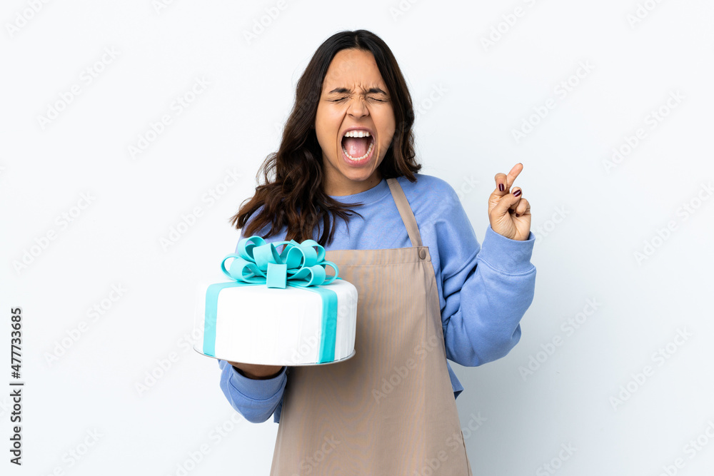 Pastry chef holding a big cake over isolated white background with fingers crossing Pastry chef holding a big cake over isolated white background with fingers crossing