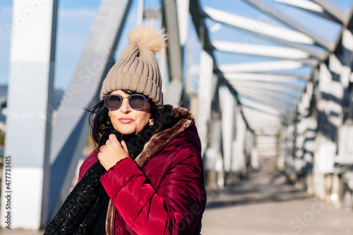 portrait of a smiling woman with sunglasses and wool cap on a sunny autumn day walking in the city