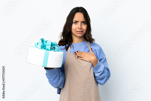 Pastry chef holding a big cake over isolated white background pointing to oneself