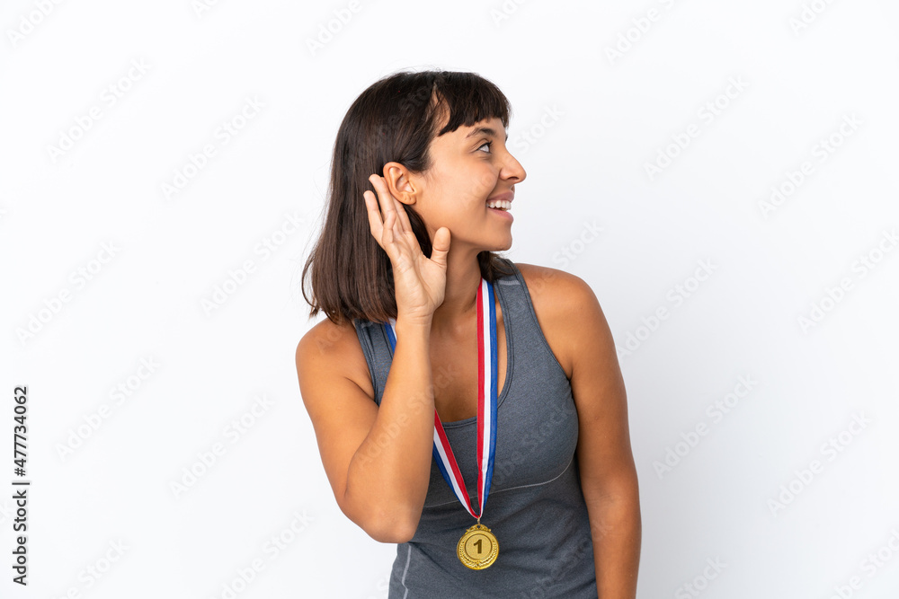 Young mixed race woman with medals isolated on white background listening to something by putting hand on the ear Young mixed race woman with medals isolated on white background listening to something by putting hand on the ear