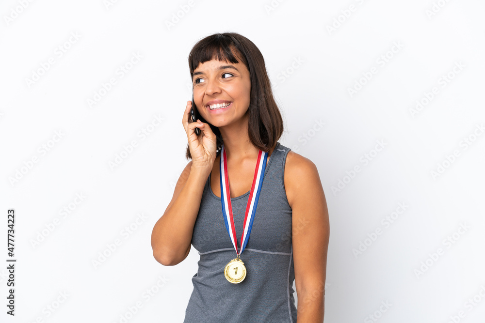 Young mixed race woman with medals isolated on white background keeping a conversation with the mobile phone Young mixed race woman with medals isolated on white background keeping a conversation with the mobile phone